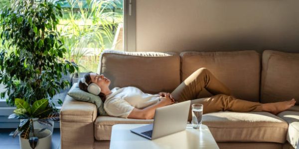 Young woman having online hypnotherapy regression session with psychotherapist lying on sofa at home. Digital service